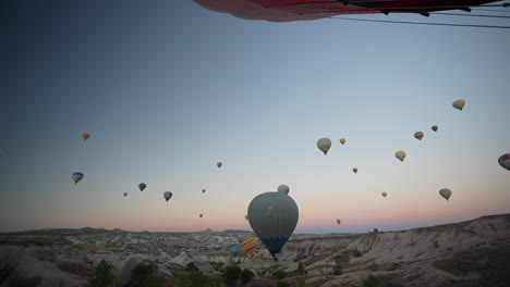 Flying-in-Hot-Air-Balloon-in-Cappadocia-Turkey,-View-of-Parachutes-From-Basket,-Tourist-Attraction-at-Dawn