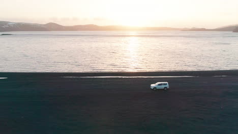 Vehicle-travelling-across-lake-Kleifarvatn-black-sand-beach-on-journey-across-Icelandic-sunset-landscape