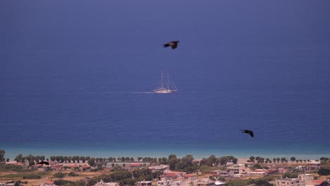 Blick-Auf-Ein-Traditionelles-Segelboot-Mit-Mast-In-Der-Ferne-Im-Mittelmeer-Vor-Rhodos-Mit-Vorbeifliegenden-Vögeln