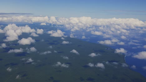 A-breathtaking-aerial-view-from-a-plane-showcases-a-lush-tropical-forest-island-surrounded-by-vast-fluffy-clouds-in-the-sky
