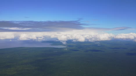 A-view-from-an-aircraft-reveals-a-lush-tropical-forest-island-surrounded-by-white-clouds
