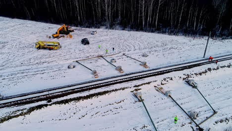 Men-And-Equipment-At-Work-At-The-Installation-Of-Utility-Poles-And-Electric-Cables-Along-Railway-On-A-Snowy-Landscape-In-Winter