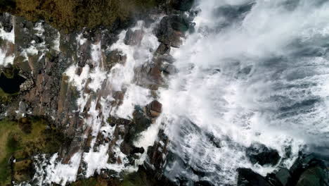 Luftaufnahme-Von-Oben-Nach-Unten-Eines-Gigantischen-Wasserfalls-Mit-Stürzendem-Wasser-Den-Berg-Hinunter-In-Den-Fluss-Während-Eines-Sonnigen-Tages---Absteigender-Schuss