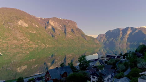 Cinematic-aerial-shot-of-of-a-Norwegian-village-in-the-mountains-and-a-mirror-of-a-still-lake-reflecting-the-mountains