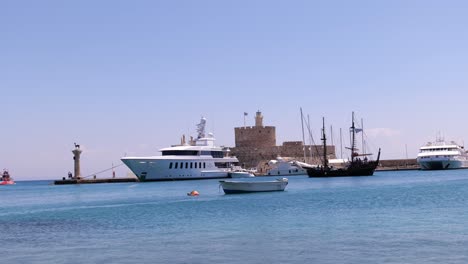 Sailing-Boat-Going-Past-Moored-Luxury-Yacht-In-Rhodes-Harbour