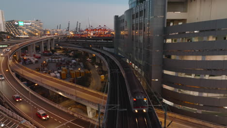 MTR-commuter-train-overpassing-highway-with-industrial-port-in-the-background-after-sunset