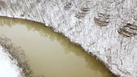 Slow-aerial-movement-over-the-brown-Kentucky-Ohio-river-during-winter-with-white-snow-everywhere