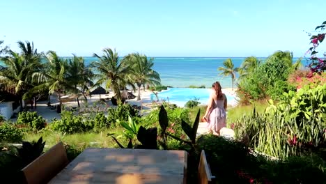 Woman-goes-down-stairs-to-an-infinity-pool-with-Indian-Ocean-view-in-luxurious-hotel-of-Zanzibar,-Tanzania