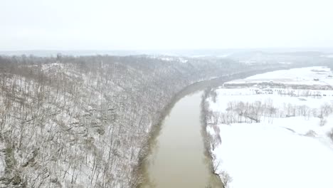 Slow-dolly-aerial-over-brown-Kentucky-Ohio-river-in-winter-with-snow-all-over-the-ground