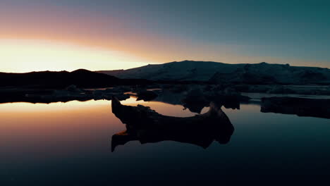 Glowing-sunset-over-striking-black-sand-beach-with-huge-glistening-iceberg-fragments,-Diamond-beach,-Iceland