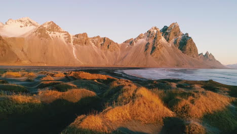 Golden-Vestrahorn-Mountain-sunrise-and-Stokksnes-low-tide-sea-grass-growing-on-black-sand-beach,-Aerial-view