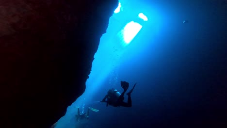 Taucher-Schwimmen-In-Einer-Unterwasserhöhle-Mit-Sonnenstrahlen-Im-Hintergrund
