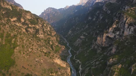 Eine-Luftdrohnenaufnahme-Einer-Schlucht-Mit-Einem-Darunter-Fließenden-Fluss-Und-Berggipfeln-Im-Hintergrund