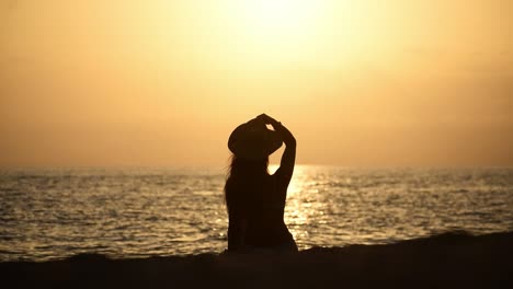 Silhouette-of-woman-relaxing,-unwinding-at-the-beach-during-sunset