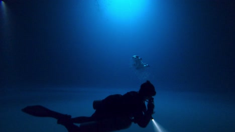 A-technical-cave-diver-calmly-floating-above-a-misty-silt-floor-with-a-torch