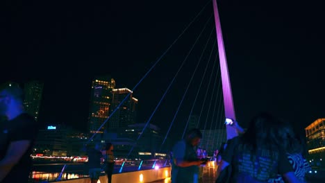 Group-Of-People-Walking-And-Taking-Pictures-On-The-Famous-Puente-de-la-Mujer-At-Night-In-Buenos-Aires,-Argentina