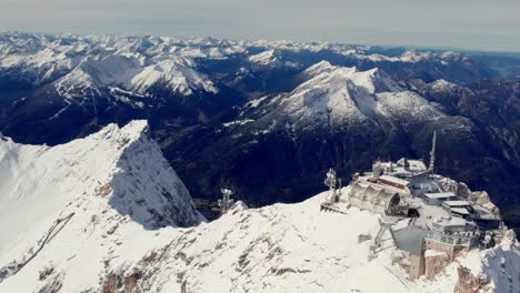 Antenne-Eines-Gebäudes-Auf-Dem-Gipfel-Eines-Gletschers,-Umgeben-Von-Schneebedeckten-Bergen-Und-Grünen-Tälern