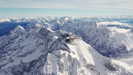 Annäherung-An-Die-Antenne-Des-Gipfels-Der-Zugspitze-Im-Winter-Mit-Schneewolken-Und-Blauem-Himmel
