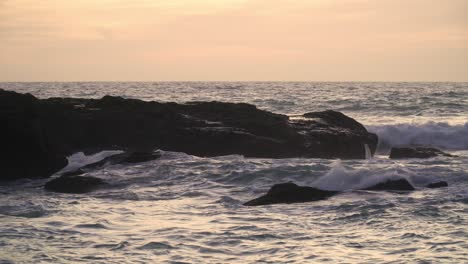 Rough-sea-with-waves-breaking-against-rocks-in-the-sea,-in-a-sunset