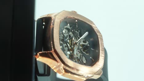 A-vertical-close-up-shot-of-a-golden-metal-hand-watch-with-a-black-band,-modern-fashion-design,-on-a-360-rotating-stand,-studio-lighting,-slow-motion,-4K-video