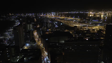 Langsame-Drohnenantenne-Von-Durban-City-Bei-Nacht-Mit-Den-Hafenlichtern-Im-Hintergrund