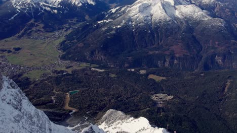 Dramática-Antena-De-Un-Valle-Forestal-Verde-Rodeado-De-Montañas-Nevadas-En-Los-Alpes