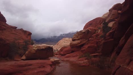 Gimbal-shot-booming-down-from-thick-clouds-to-natural-desert-water-tank-in-Red-Rock-Canyon,-Nevada