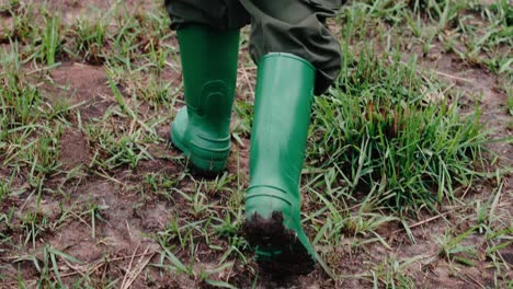 Person-walks-over-muddy-landscape-with-green-rain-boots
