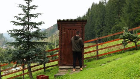 Man-Opens-The-Door-And-Enters-A-Rustic-Wooden-Outdoor-Toilet