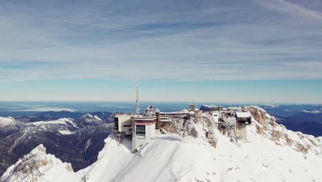 Umlaufende-Antenne-Des-Schneebedeckten-Berggipfels-Mit-Grünem-Tal-Darunter-Und-Bergketten-Im-Hintergrund