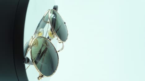 A-vertical-close-up-cinematic-shot-of-laying-golden-sunglasses-on-a-360-rotating-reflecting-stand,-studio-light,-product-4K-video,-slow-motion