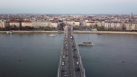Aerial-view-of-Traffic-at-Bridge-above-River-Danube-During-Sunset-at-Budapest-with-the-City-in-the-Background