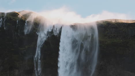 Mist-from-reverse-waterfall-in-Iceland-blows-over-top-of-majestic-cliff