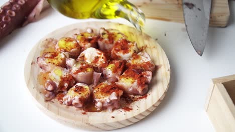 Octopus-seasoned-with-paprika,-pouring-some-olive-oil-to-temper-and-prepare-it-for-cooking,-on-a-wooden-cutting-board-and-white-table