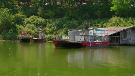 Tiro-De-Casas-Flotantes-A-Lo-Largo-De-La-Orilla-Del-Lago-En-El-Pueblo-De-Pescadores-De-Pak-Nai,-Provincia-De-Nan,-Tailandia-Con-Vegetación-Verde-En-El-Fondo-Durante-El-Día