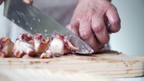 Caucasian-person-with-old-hands-and-white-apron-cutting-octopus-tentacles-to-be-cooked,-on-a-wooden-board
