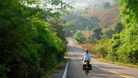 Vista-Trasera-De-Mujeres-Montando-En-Bicicleta-En-La-Carretera-Del-Pueblo-De-Pescadores-De-Pak-Nai,-Provincia-De-Nan,-Tailandia