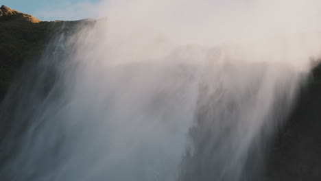 Mist-from-large-waterfall-cyclone-blows-over-cliff-in-high-winds,-Iceland