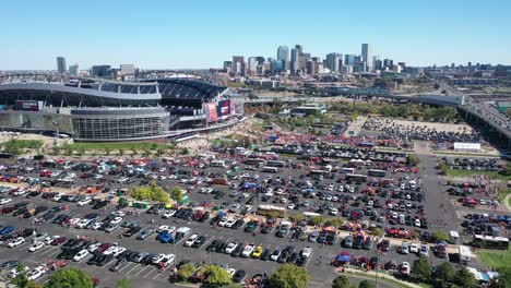 Cinematic-aerial-shot-of-Empower-field-at-Mile-High-Stadium-with-lots-of-cars-parked-in-parking-spaces-and-main-street-highway-and-Downtown-Denver-city-view-backdrop,-Colorado