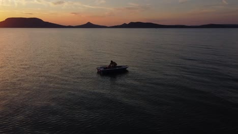 Luftaufnahme-Eines-Jungen-Paares-In-Einem-Boot,-Das-Bei-Sonnenuntergang-Auf-Dem-See-Schwimmt,-Mit-Bergen-Im-Hintergrund