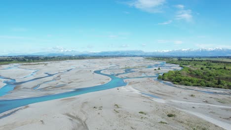 Flying-high-upstream-over-braided-Waimakariri-River-in-New-Zealand---numerous-channels-of-beautiful-turquoise-water,-clear-blue-sky-and-mountains-in-distance