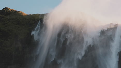 Mist-from-large-waterfall-cyclone-swirls-and-blows-around-rugged-cliff,-Iceland
