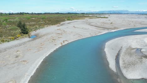 Flying-low-upstream-over-main-channel-in-beautiful-turquoise-colored-Waimakariri-River,-New-Zealand---revealing-mountains-on-low-horizon