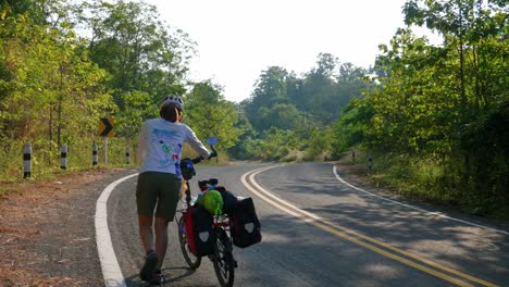 Vista-Trasera-De-Mujeres-Caminando-Con-Bicicleta-En-El-Camino-Forestal-De-La-Aldea-De-Pescadores-De-Pak-Nai,-Provincia-De-Nan,-Tailandia