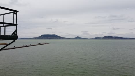 Aerial-View---Passing-by-a-Storm-SIgnal-Pillar-at-Lake-Balaton-with-Mountains-in-the-background