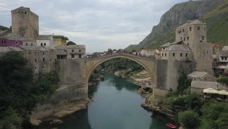 Tourists,-locals-gather-on-Mostar-old-bridge-high-over-Neretva-River