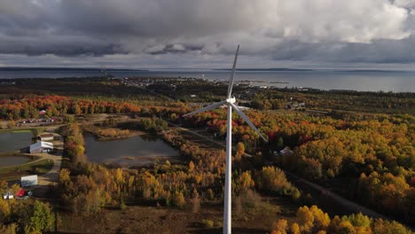 Mackinaw-township-in-horizon-while-wind-turbine-spin-in-foreground,-aerial-view