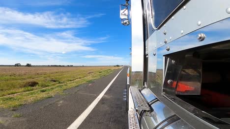 Shot-taken-from-the-side-of-a-truckload-towards-the-road,-landscape-with-low-vegetation-and-blue-sky-with-clouds-on-the-horizon