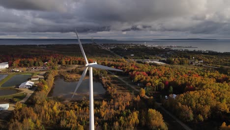 Wind-turbine-spinning-with-view-of-Mackinac-bridge-and-township-on-horizon,-aerial-view