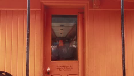 Vintage-orange-passenger-train-revealed-through-handheld-shot,-tight-close-up-from-exterior-while-in-motion,-swaying